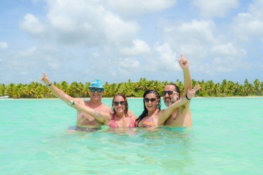 A group of people in a turquoise ocean with palm trees in the background. 1