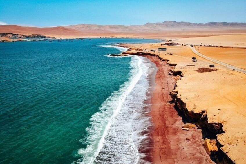 A coastal landscape with a sandy beach, a clear blue sea, and distant mountains. 2