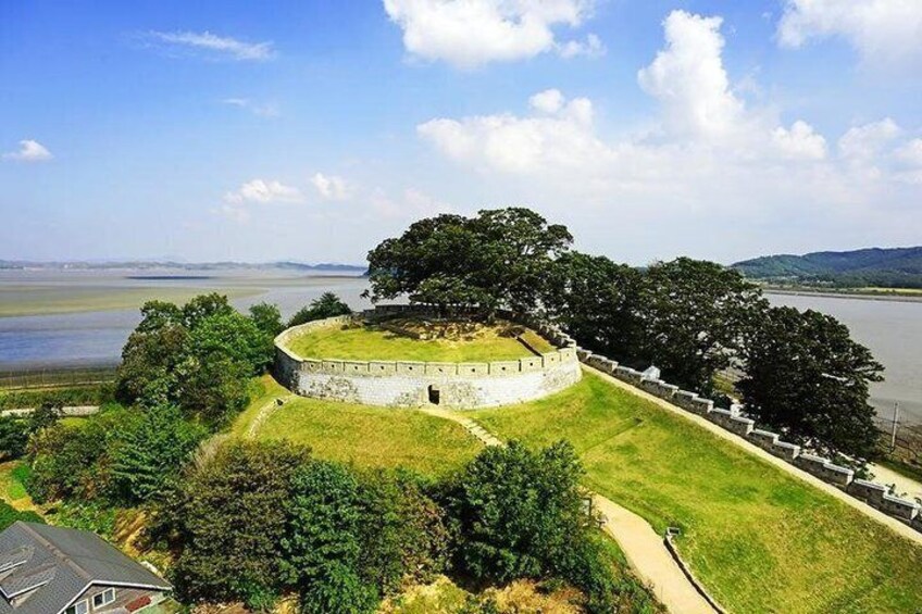 A historical fort with a grassy mound, surrounded by trees and a body of water. 3