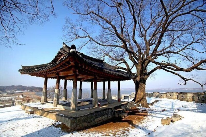 A traditional pavilion with a tiled roof, a large tree, and snow-covered ground. 4