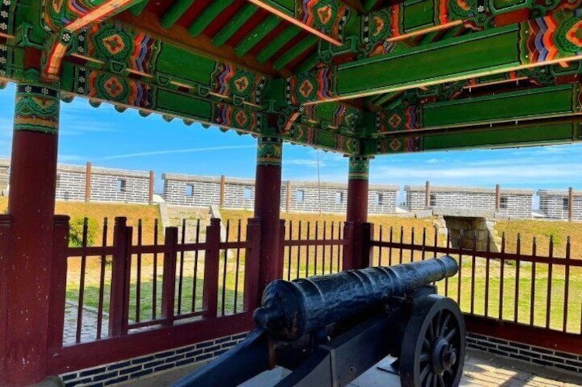 A cannon in a pavilion with a view of a fort. 2