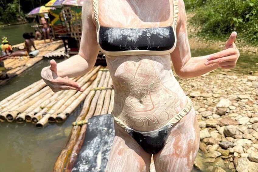 A person in a swimsuit with a design on their midsection, standing on a bamboo raft in a river. 4