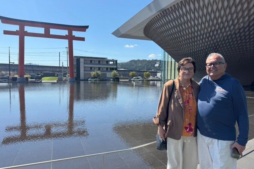Two people standing in front of a modern building with a red torii gate in the background. 2