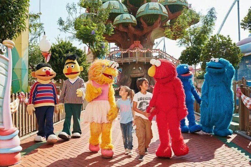A group of characters from a children's show interacting with children on a paved pathway. 3