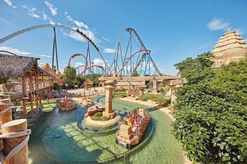 A water park with a roller coaster, a central fountain, and a thatched-roof pavilion. 4
