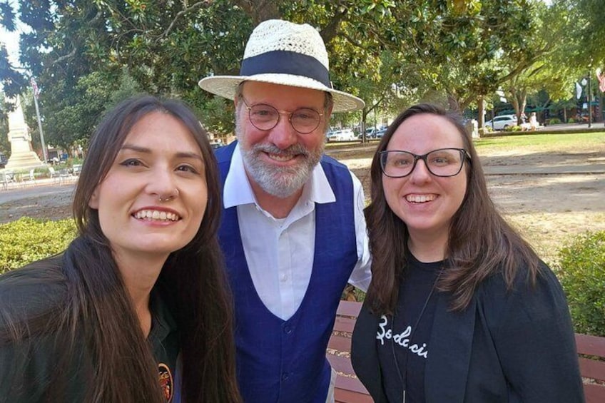 Three people in a park with a statue and trees in the background. 3