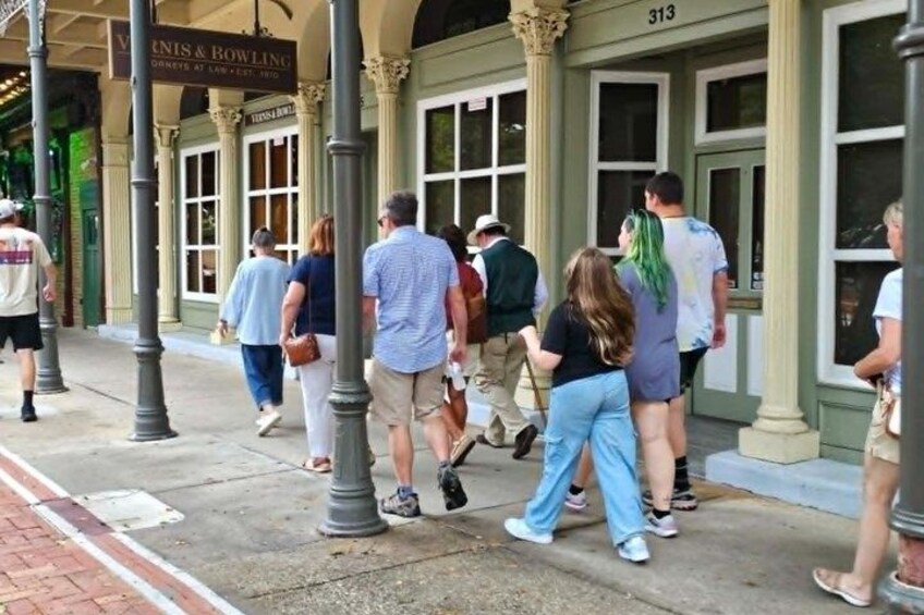 A group of people walking on a sidewalk in front of a building with columns and a sign that reads 'VINN'S & BOWLING'. 2