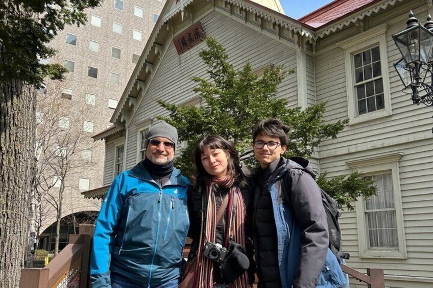 Three people standing in front of a building with a red roof and white siding. 2
