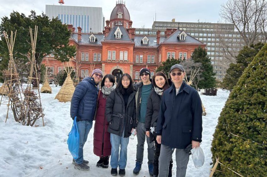 A group of people standing in a snowy area with a large red building in the background. 5