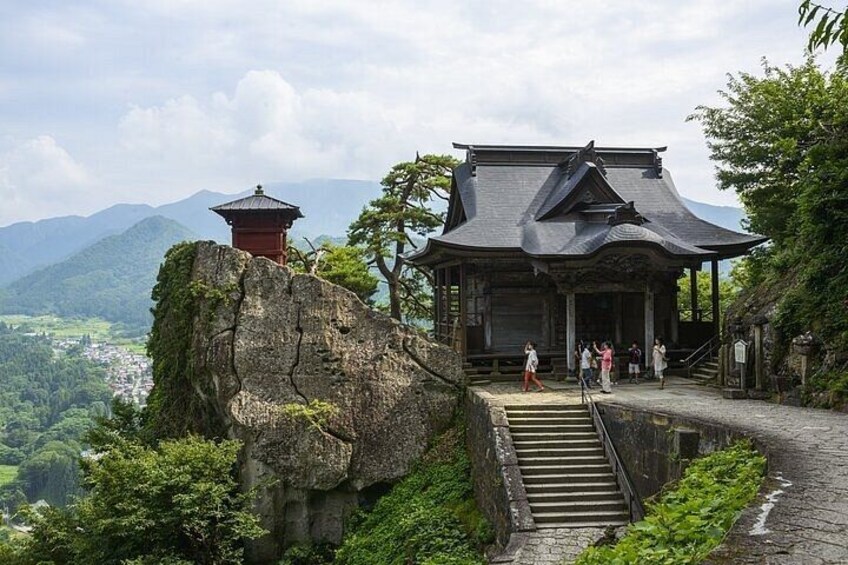 A traditional Japanese temple on a mountain, with a stone staircase leading up to it. 4