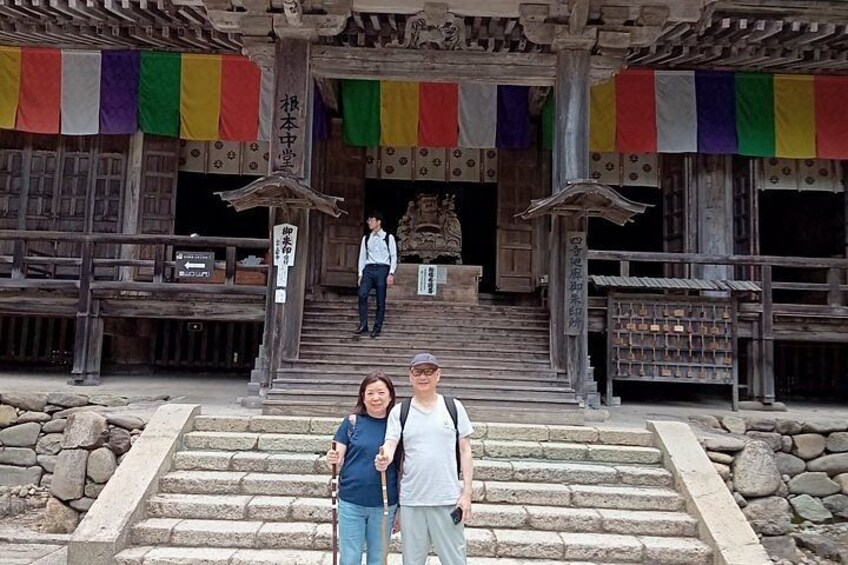 A traditional wooden structure with steps leading up to a shrine, colorful flags, and a person standing at the top. 5