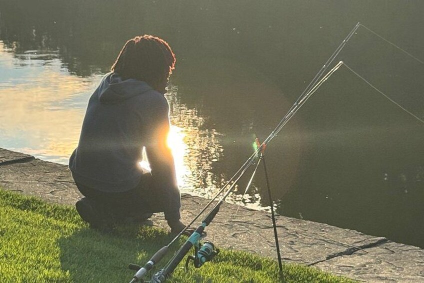 A person fishing by a calm body of water during sunset. 3