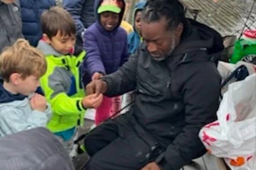 A person sitting outdoors with children around, possibly in a public space. 3