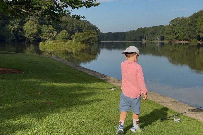 A person fishing by a calm lake surrounded by trees. 4