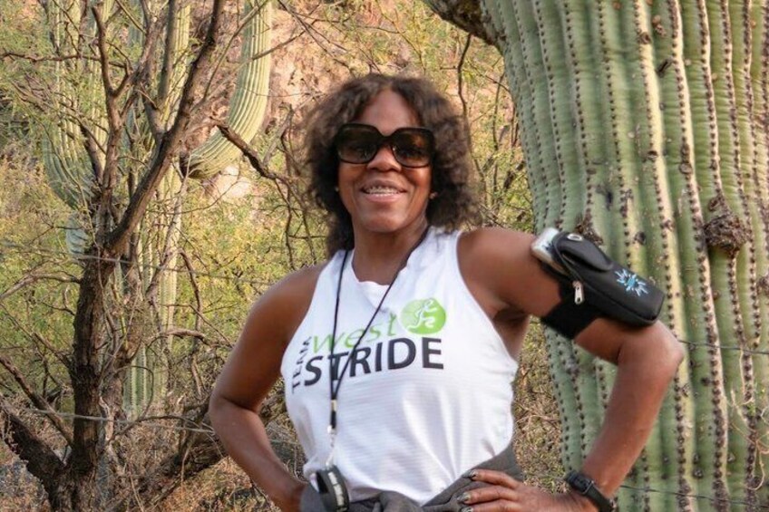 A person wearing a white tank top with 'WCS STRIDE' printed on it, standing outdoors with a cactus and dry vegetation in the background. 5
