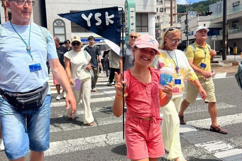 A group of people crossing a street, a blue banner with white letters, and a building in the background. 5