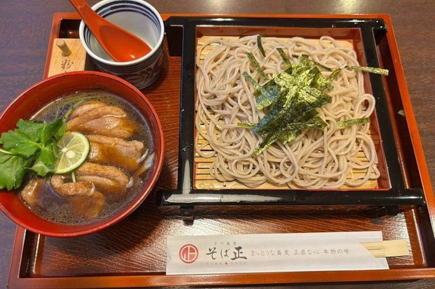 A bowl of soup with meat and a plate of noodles garnished with seaweed. 3