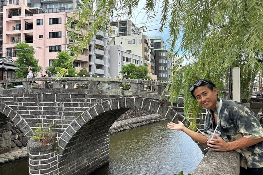 A stone bridge over a river, a person leaning on the bridge railing, and buildings in the background. 2