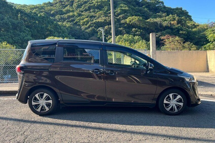 A dark-colored minivan parked on a paved surface with a mountainous background. 4