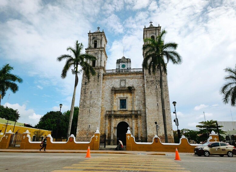 A historic stone building with two towers, palm trees, and a pedestrian crossing. 3