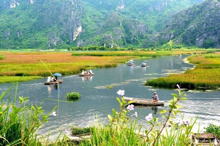 A river with boats, lush greenery, and rocky mountains in the background. 1