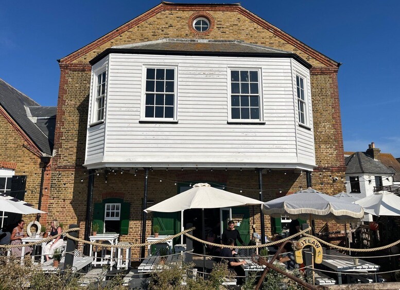 A white building with a brick facade, a round window, and a covered outdoor seating area with umbrellas. 5