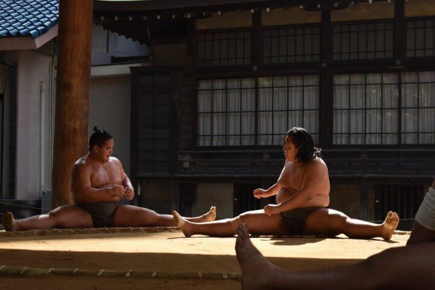 Two sumo wrestlers sitting on tatami mats in a traditional Japanese building. 1