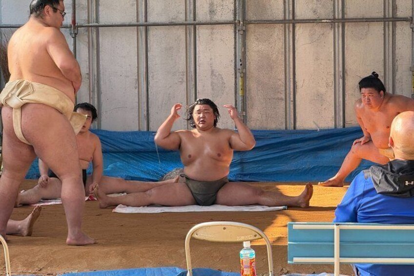 A group of sumo wrestlers sitting on a mat, with one wrestler in a relaxed pose. 2