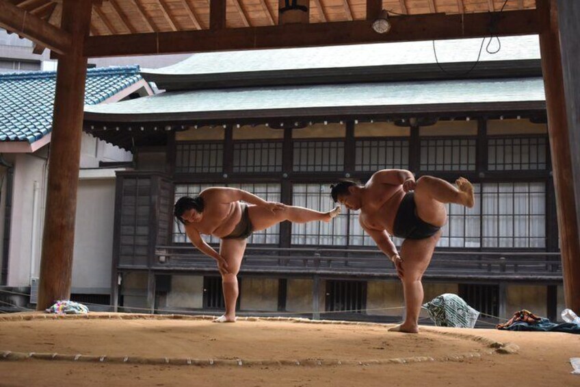 Two sumo wrestlers practicing in a traditional Japanese setting with wooden architecture and a dirt floor. 5