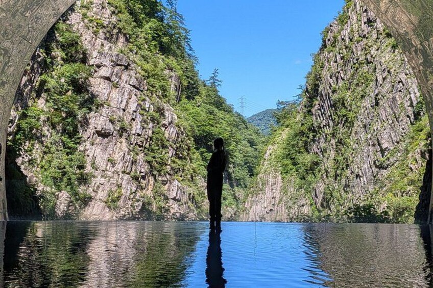 A person standing in a river with rocky cliffs on either side. 1