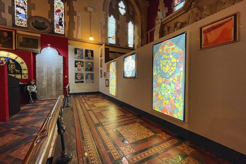 A church interior with stained glass windows, a wooden floor, and religious artwork on the walls. 5