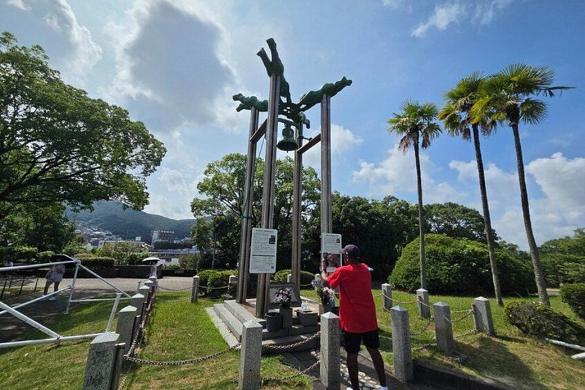A person taking a photo of a bell tower with a chain fence in a park with palm trees and a mountain in the background. 3