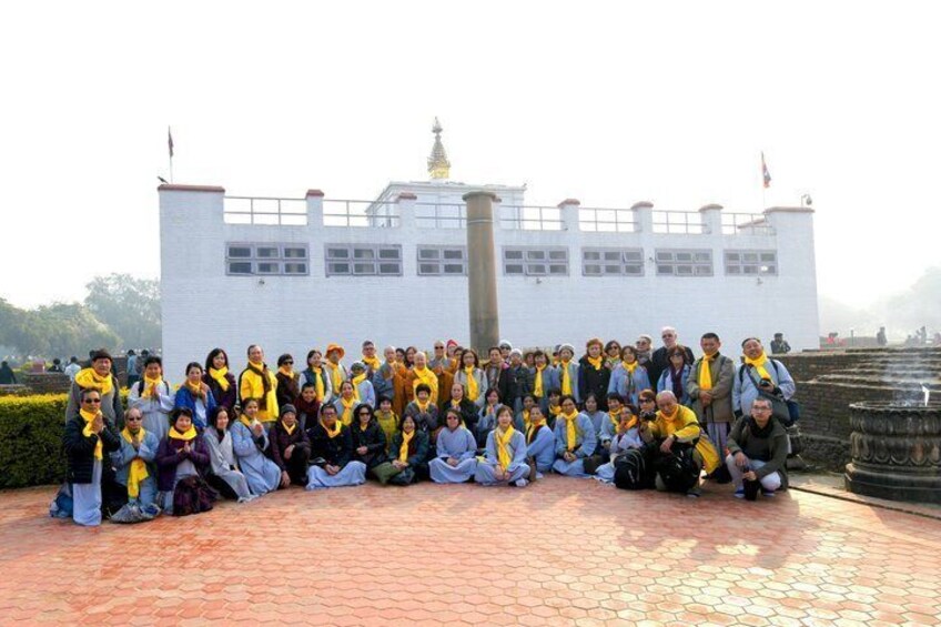 A group of people gathered outdoors in front of a white building with a flag on top. 1