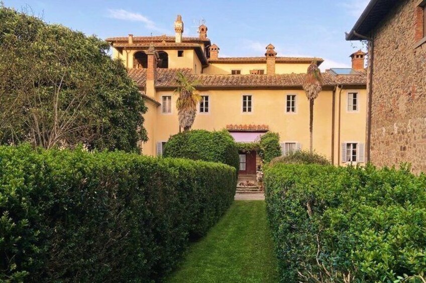A yellow building with a tiled roof, surrounded by well-maintained hedges and a clear sky. 2