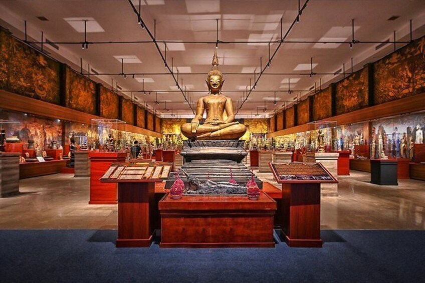 A large golden Buddha statue in a spacious hall with red display cases and a blue carpet. 3