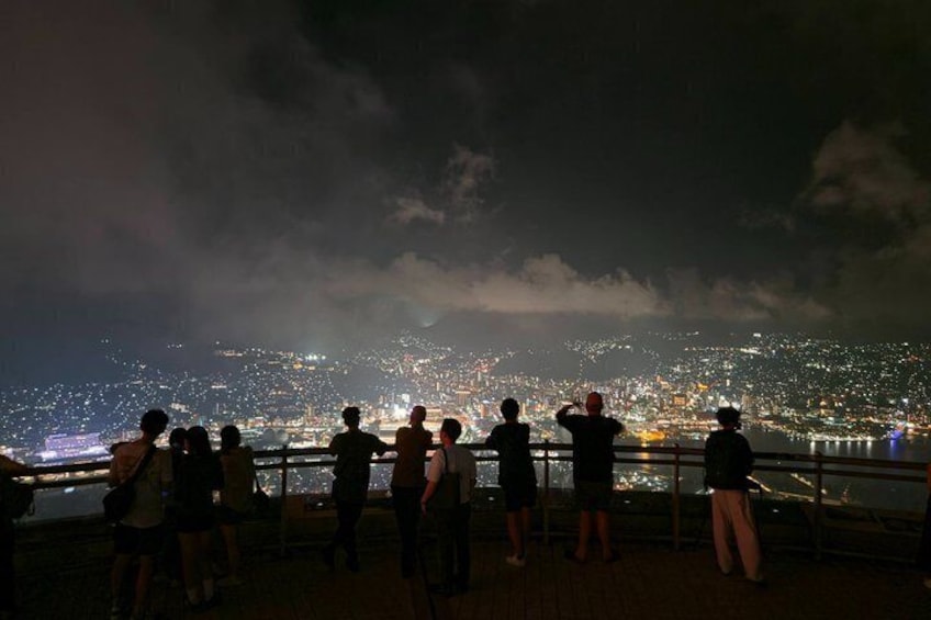 A group of people standing on a balcony overlooking a cityscape at night. 5