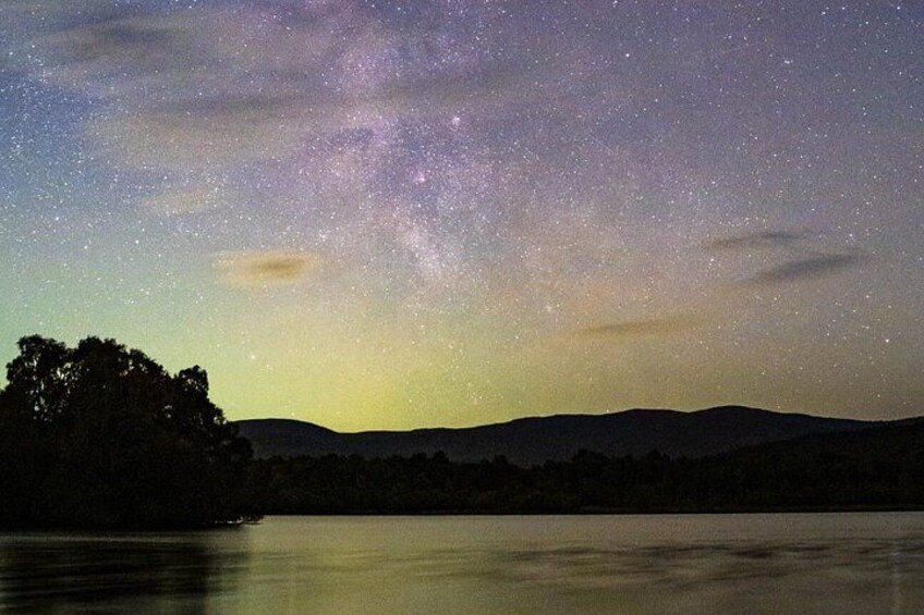 A starry night sky over a calm lake with silhouetted trees and distant hills. 5