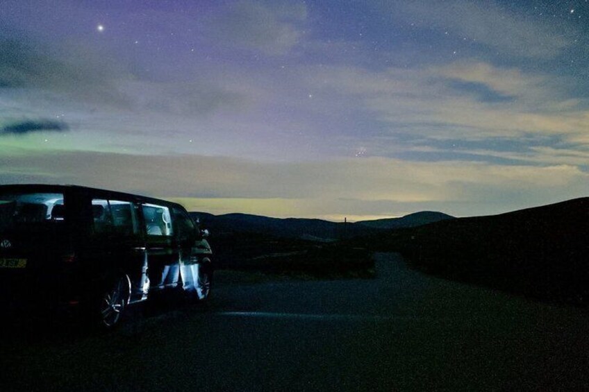 A van parked on a road at night with a starry sky above. 2