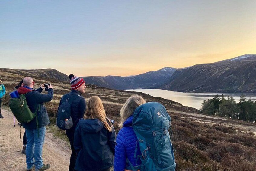 A group of people standing on a path, overlooking a lake and mountains. 2