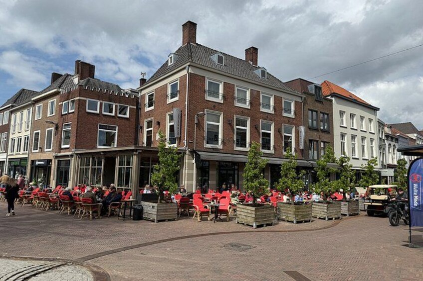 A street with red chairs and tables, brick buildings, and a blue sign. 3