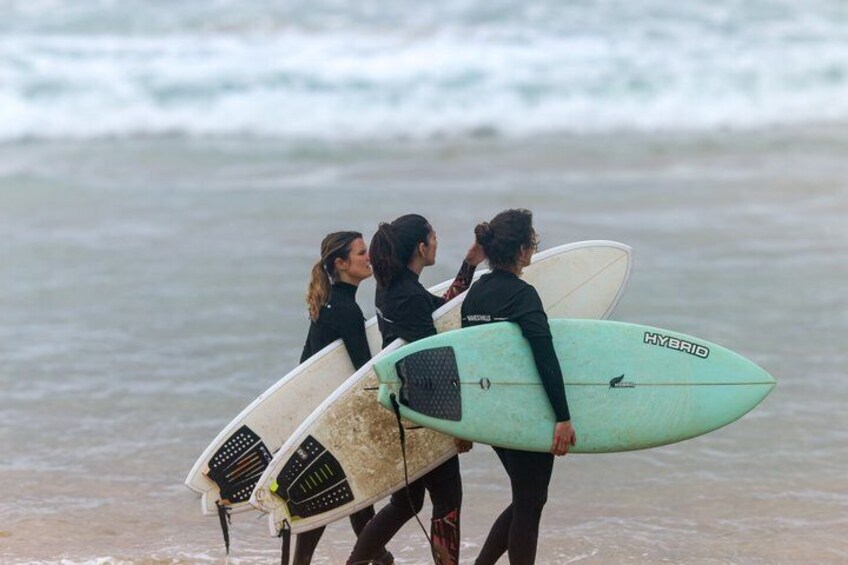 Three people walking on a beach, each holding a surfboard. 4