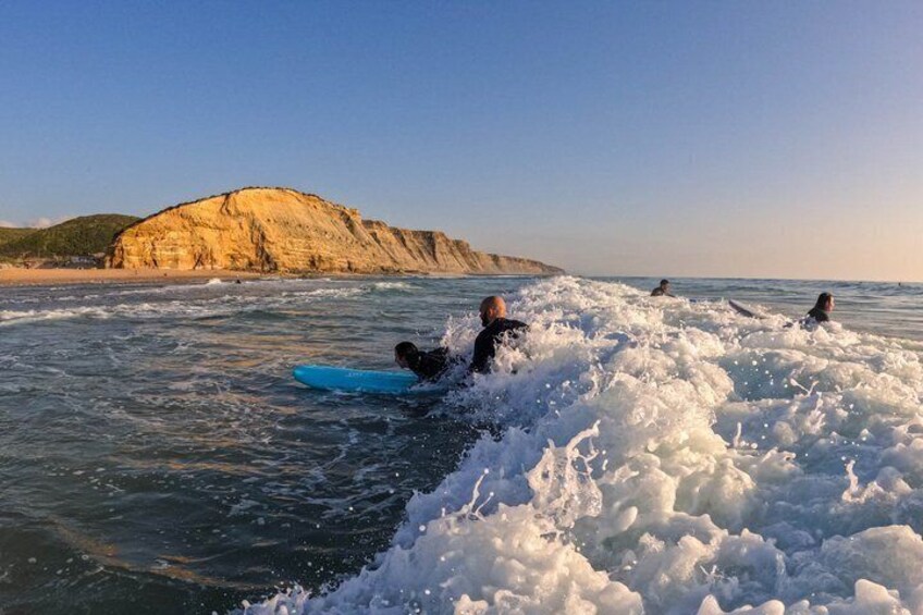 A person surfing in the ocean with waves and a cliff in the background. 1