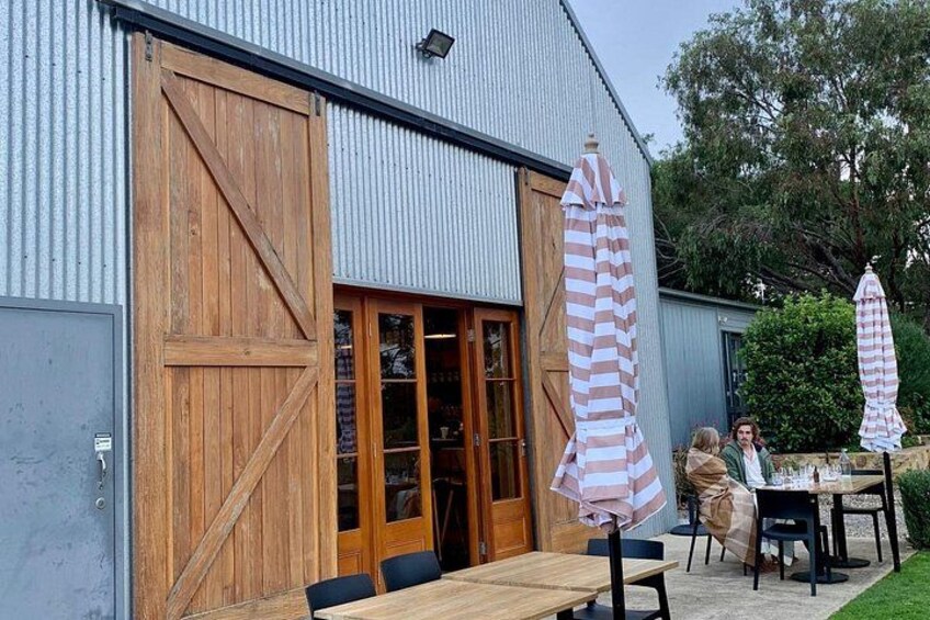 A rustic building with large wooden doors and windows, outdoor seating with striped umbrellas, and a well-maintained lawn. 2