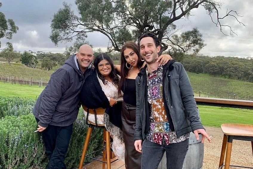 A group of people standing outdoors with a vineyard in the background. 5
