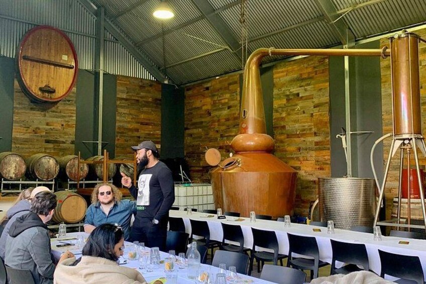 A distillery with large copper stills, wooden barrels, and a brick wall. 3