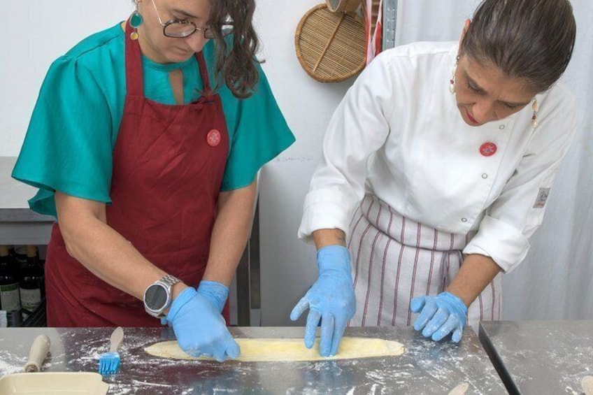 Two people wearing aprons and gloves working with dough on a table. 5