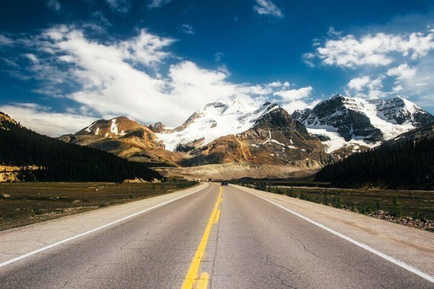 A road leading towards snow-capped mountains under a clear sky. 5