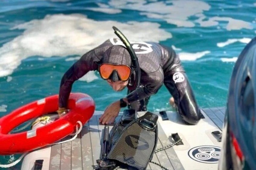 A person in a wetsuit and diving mask on a boat, preparing to enter the water. 4