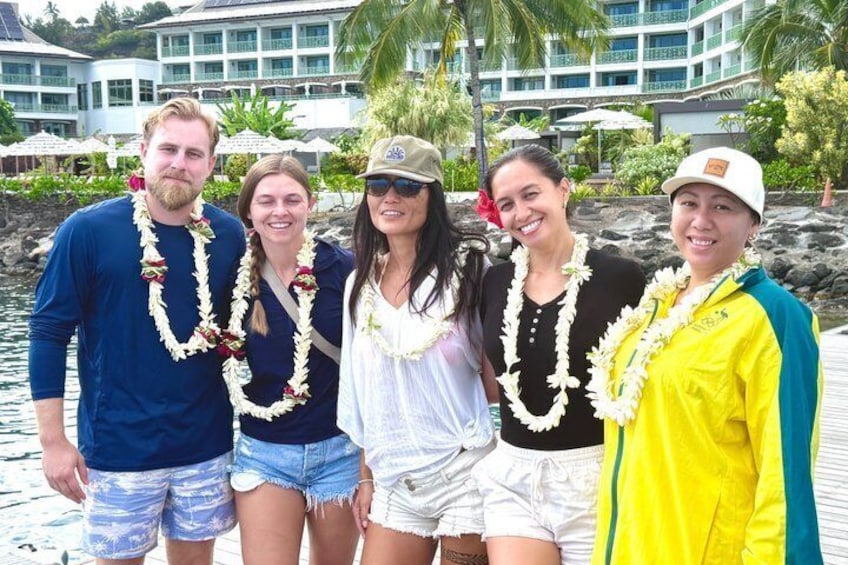 A group of people standing by a waterfront with a building and palm trees in the background. 2