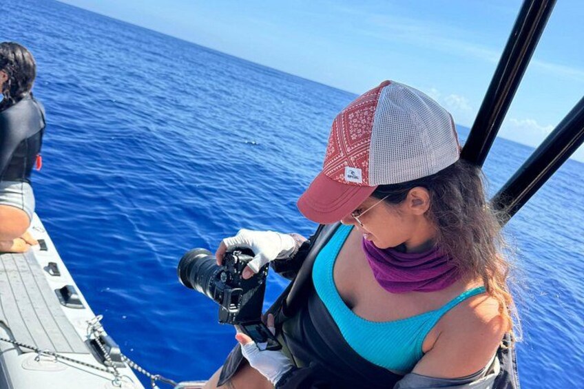 A person on a boat holding a camera, with the ocean in the background. 2